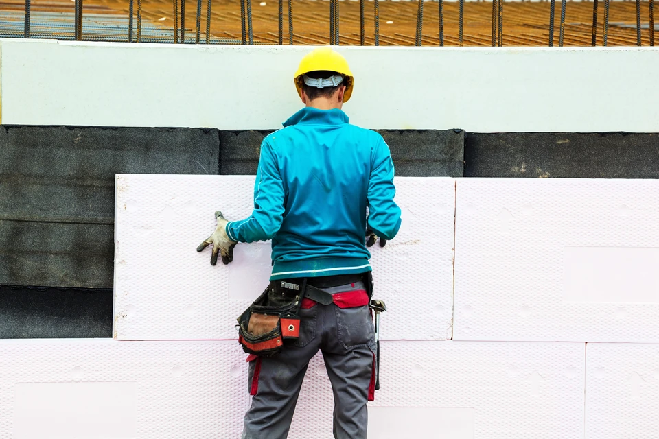 Ouvrier en construction appliquant des panneaux d'isolation thermique sur mur extérieur