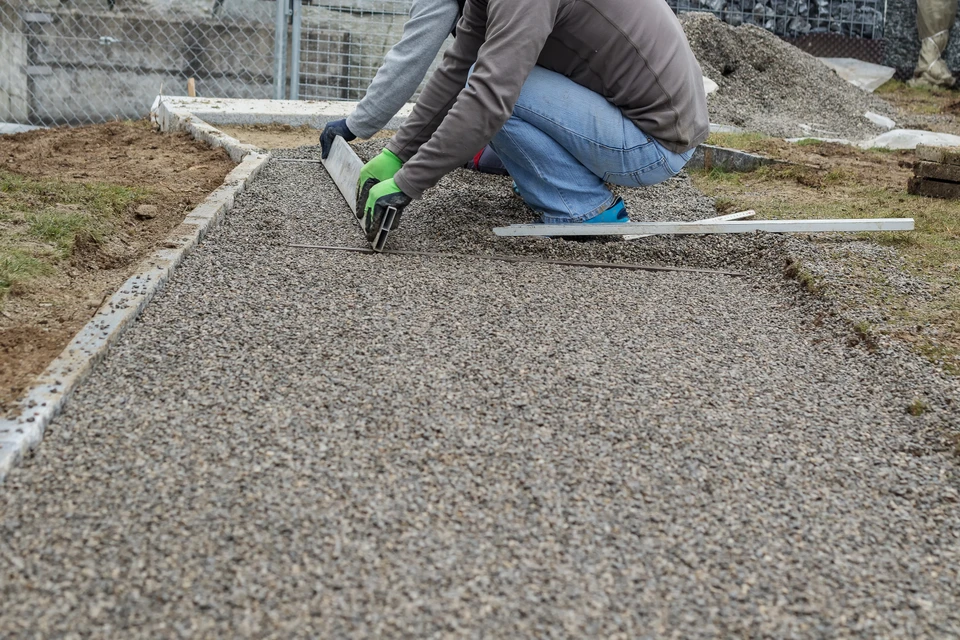 Chantier extérieur, ouvrier à genoux nivelle une surface granulaire avec une règle métallique