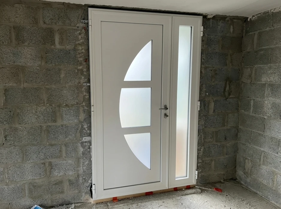 Pose d'une porte d'entrée en PVC blanc dans une maison en construction, murs en parpaings apparents