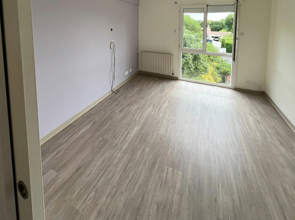 Pièce vide avec sol en vinyle LVT imitation bois gris clair, murs blanc-lavande, plinthe blanche