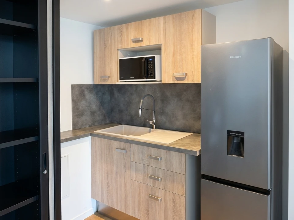 Entrée moderne d'une maison contemporaine avec porte d'entrée en bois clair à lames verticales, escalier en pierre naturelle beige, façade en bardage métallique bleu foncé nervuré